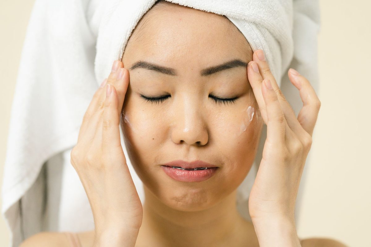 Application d'un soin hydratant sur le visage, serviette sur les cheveux