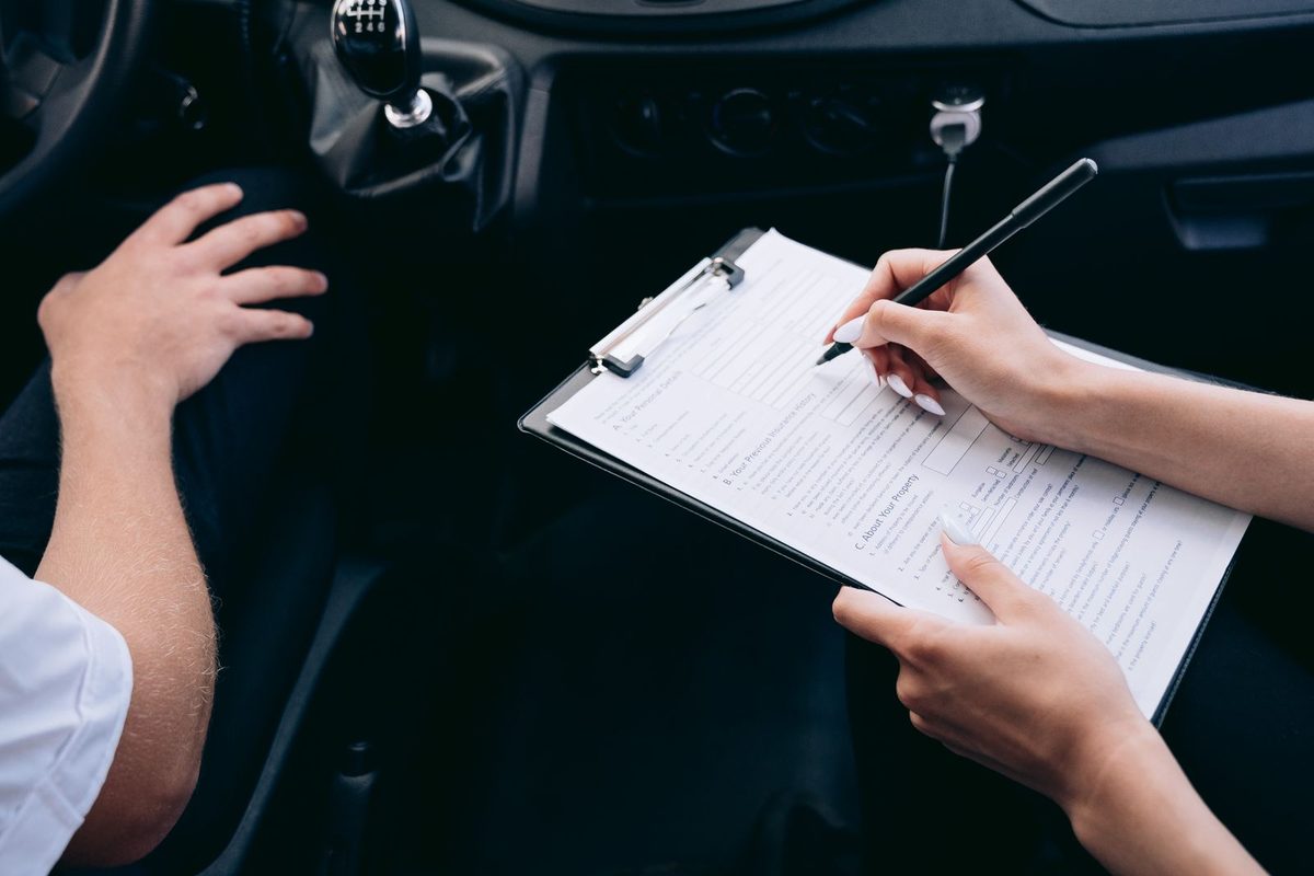Main remplissant un document appuyée sur le volant d'une voiture