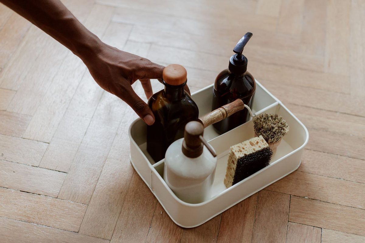 Main saisissant un flacon dans un caddie de produits d'entretien posé au sol