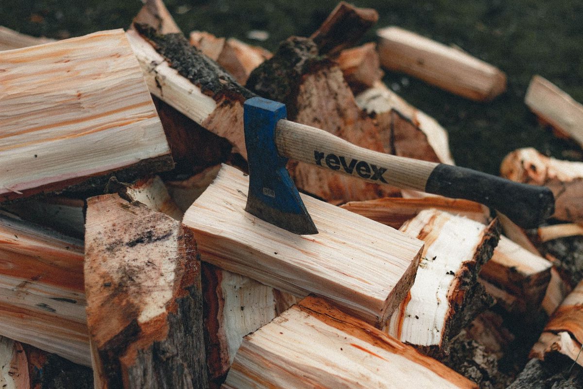 Hache plantée dans une bûche, devant un tas de bois fendu