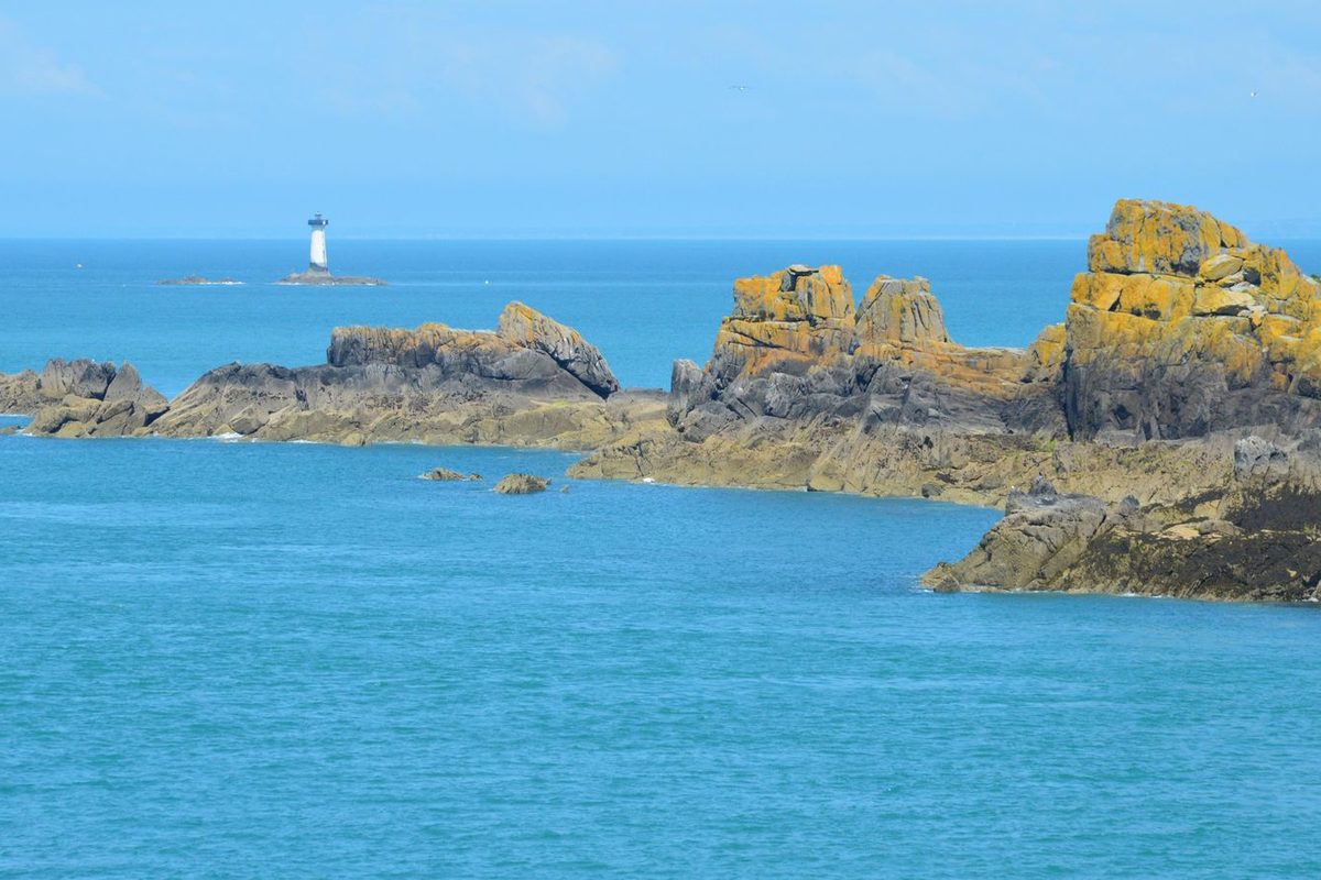 Rochers de granit et phare blanc sur la côte bretonne, face à une mer turquoise