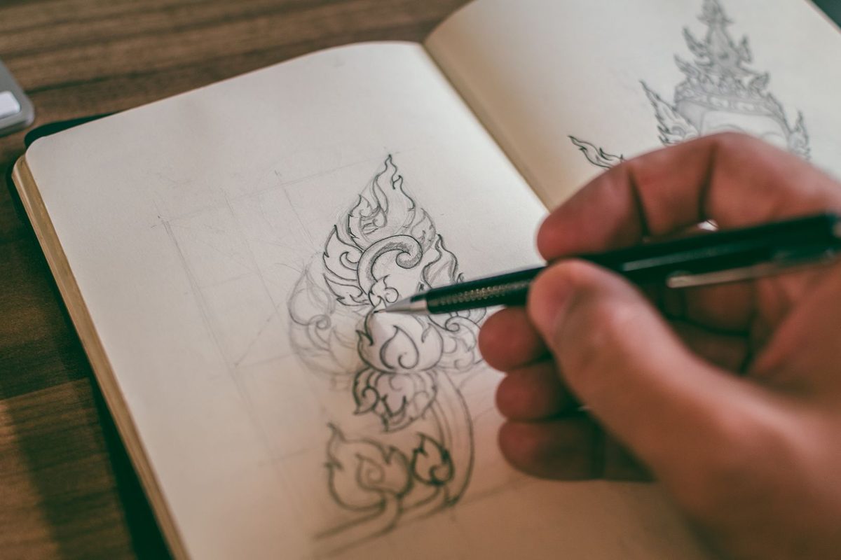 Main dessinant un motif au crayon sur un carnet de croquis