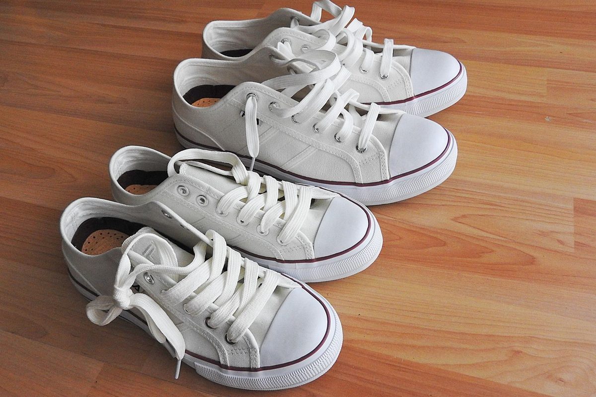 Plusieurs paires de baskets blanches alignées sur un parquet