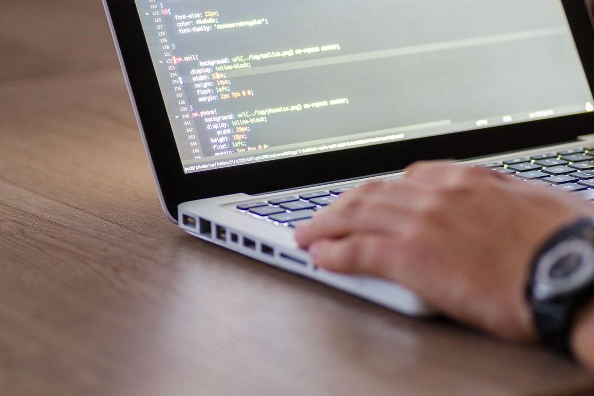Mains sur le clavier d'un portable affichant des lignes de code