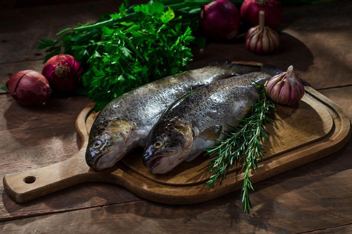 Deux poissons entiers sur une planche, avec herbes et aromates