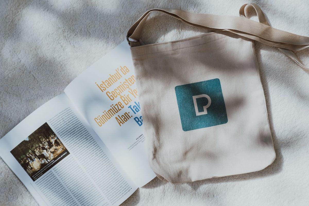 Tote bag en lin marqué d'un logo, posé près d'un magazine ouvert