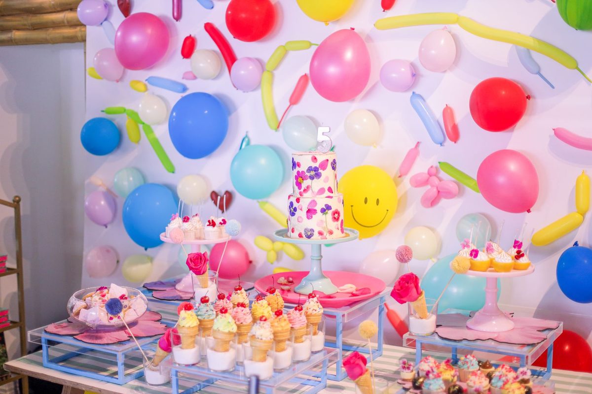 Table d'anniversaire garnie de gâteaux, sous un mur de ballons colorés