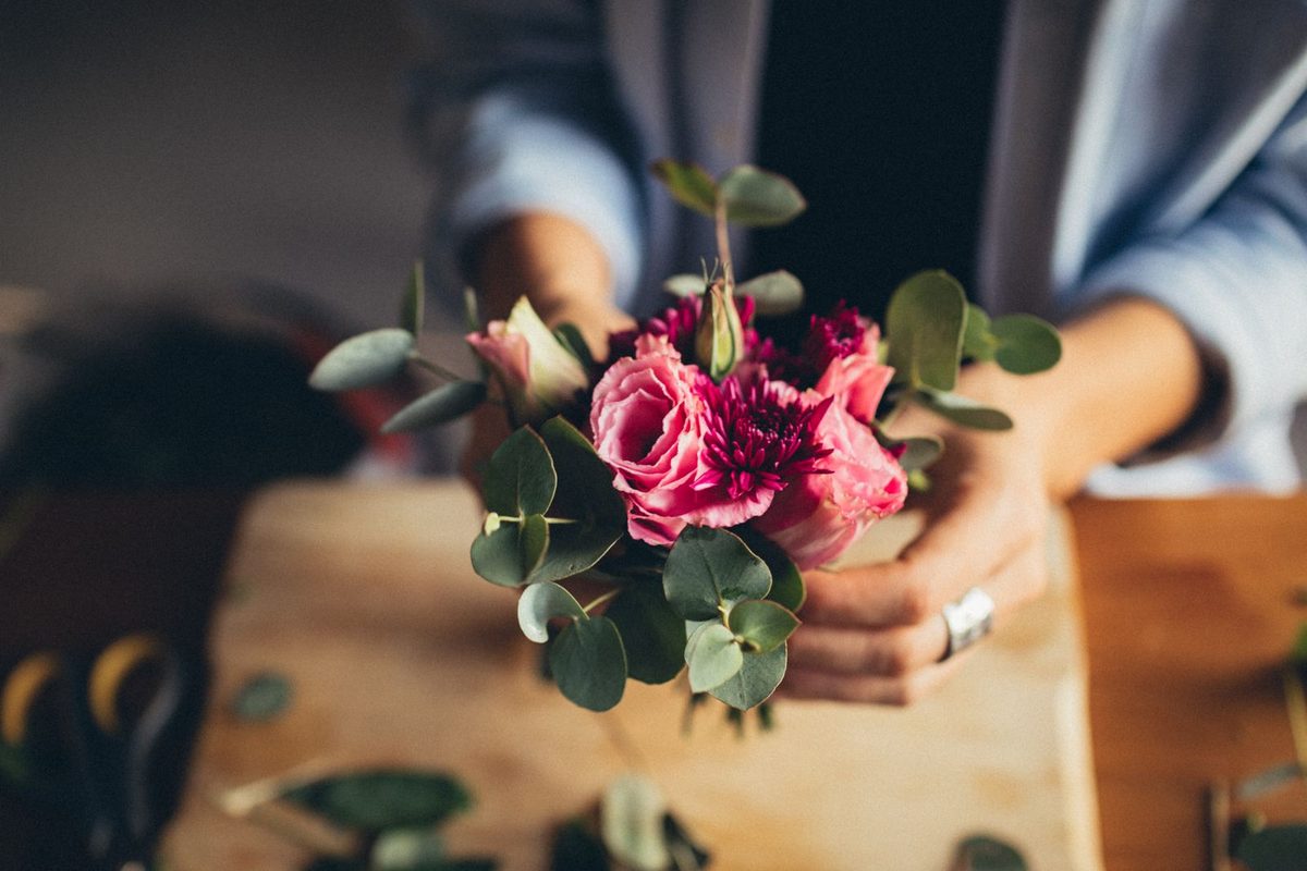 Mains composant un bouquet de roses et d'eucalyptus sur un plan de travail