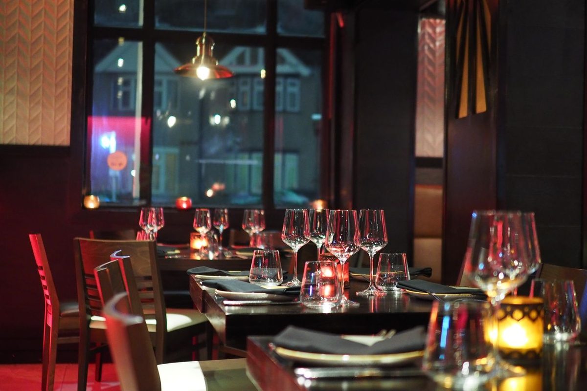 Salle de restaurant dans la pénombre, tables dressées aux chandelles