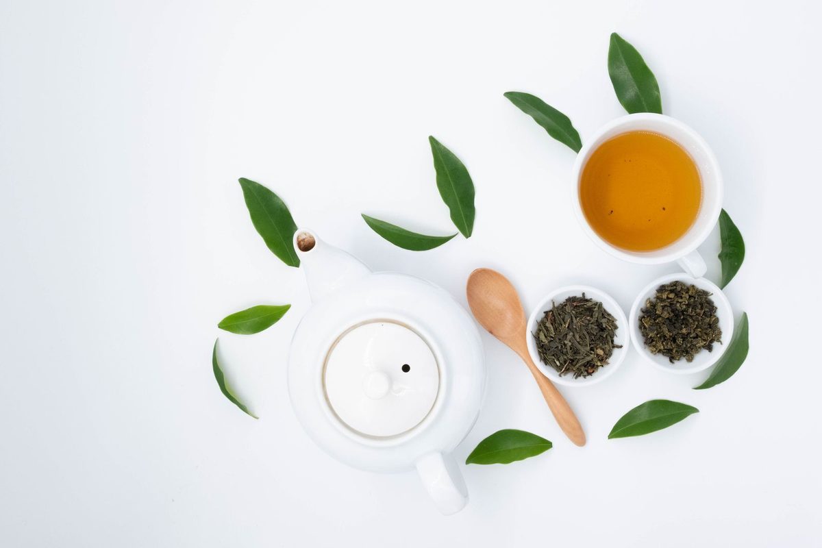 Tasse de thé vert, théière et feuilles séchées sur une table claire