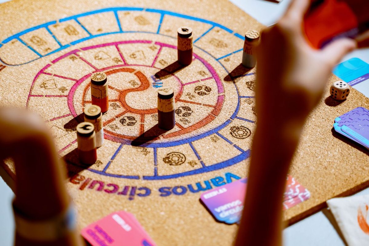 Plateau de jeu coloré avec pions, autour duquel plusieurs mains jouent