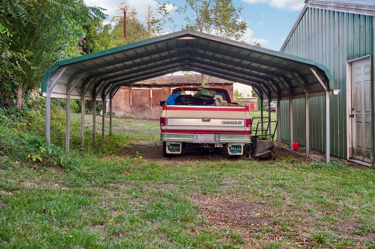 Voiture stationnée sous un carport en bois adossé à un bâtiment