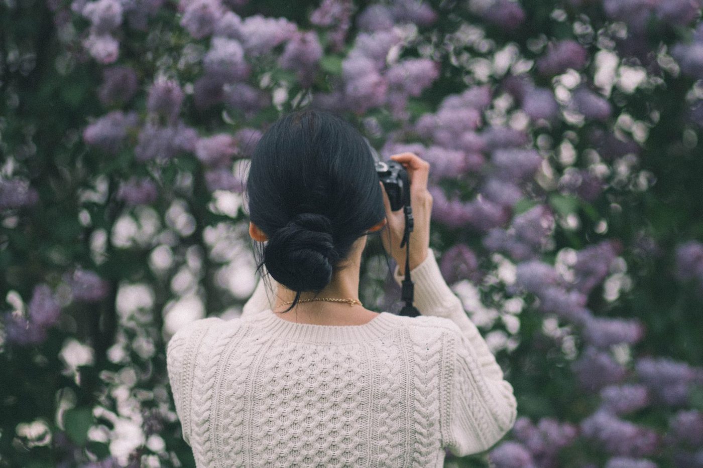 Femme coiffée d'un chignon bas devant un massif de lilas en fleurs