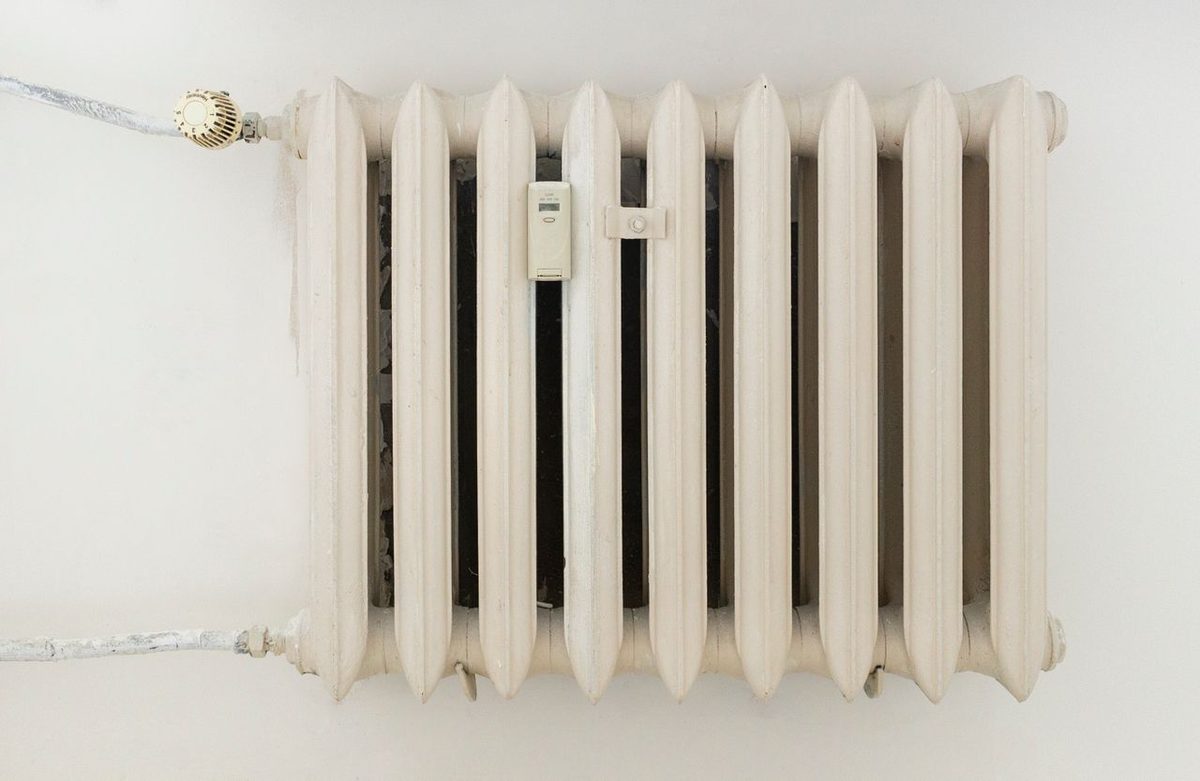 Radiateur blanc à ailettes fixé sur un mur clair